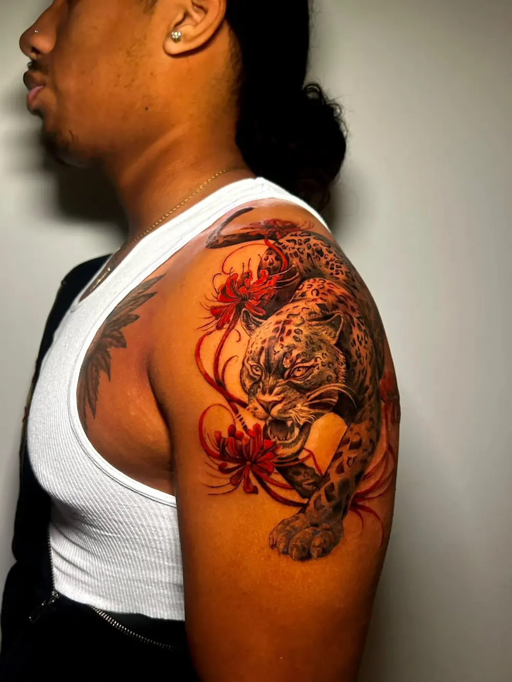 Snarling jaguar in black and grey on a shoulder, with red spider lilies