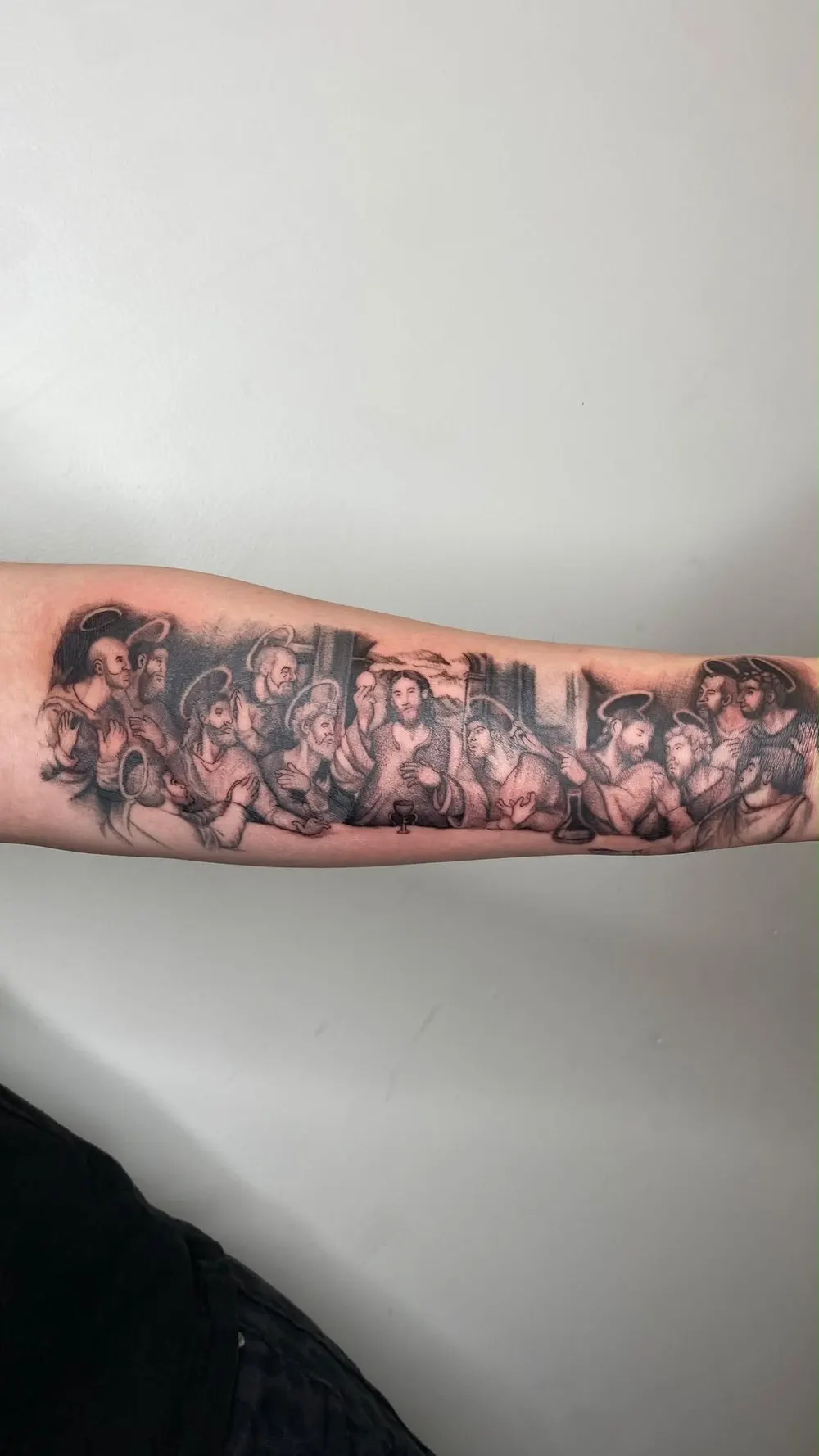 Black and grey Last Supper tattoo running the length of a forearm