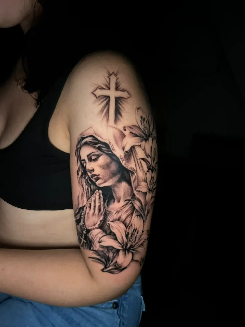 Virgin Mary praying with rosary, lilies and a cross, on an upper arm